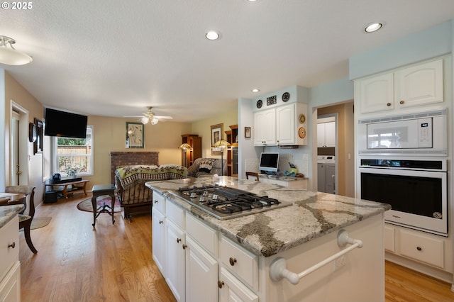 kitchen with white appliances, open floor plan, light stone counters, light wood finished floors, and a center island