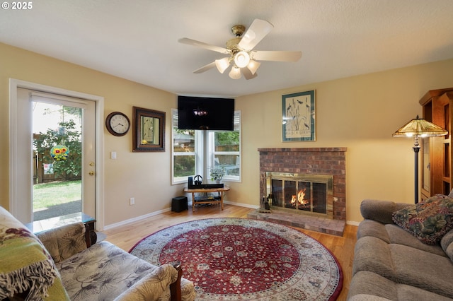 living room featuring a brick fireplace, wood finished floors, and a ceiling fan