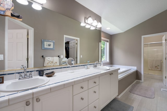 bathroom featuring a stall shower, vaulted ceiling, baseboards, double vanity, and a garden tub