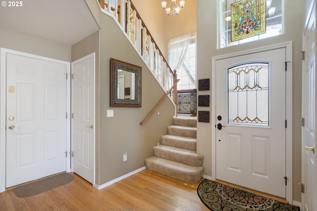 foyer featuring light wood-style flooring, stairs, a chandelier, baseboards, and a high ceiling