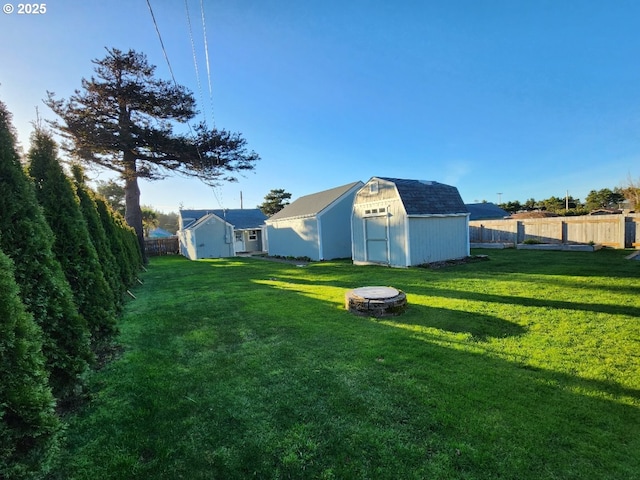 view of yard featuring a storage shed, a fenced backyard, a fire pit, and an outbuilding