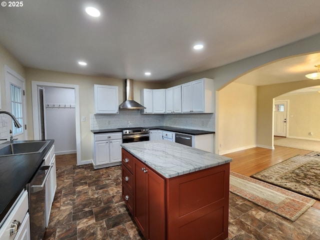 kitchen featuring tasteful backsplash, arched walkways, wall chimney exhaust hood, stainless steel appliances, and a sink