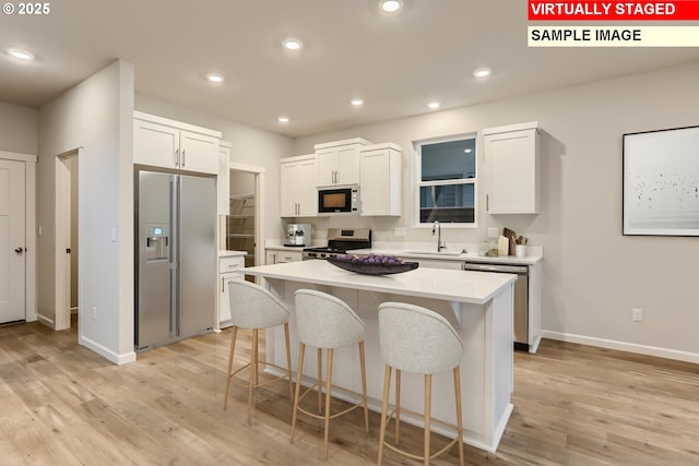 kitchen with a breakfast bar area, recessed lighting, appliances with stainless steel finishes, light wood-style flooring, and a sink