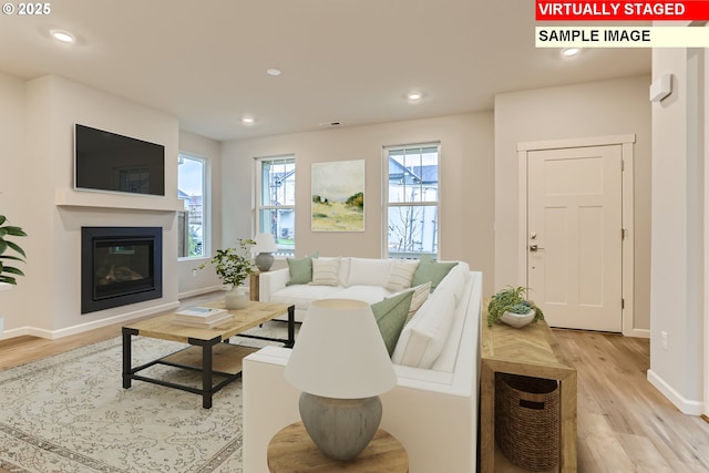 living area with a glass covered fireplace, recessed lighting, light wood-type flooring, and baseboards