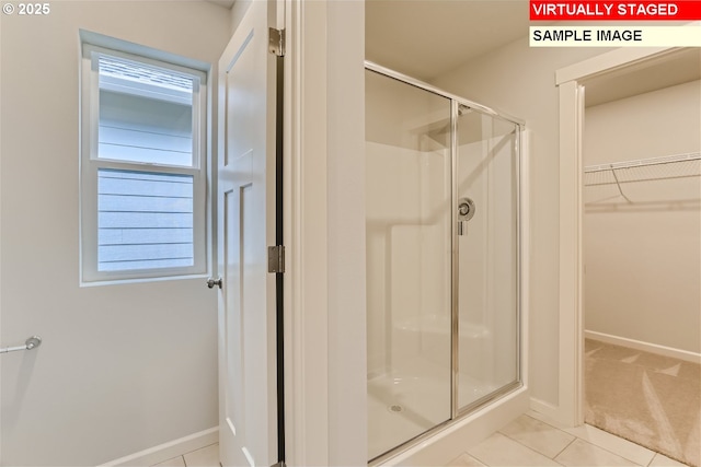 bathroom featuring a walk in closet, baseboards, a stall shower, and tile patterned flooring