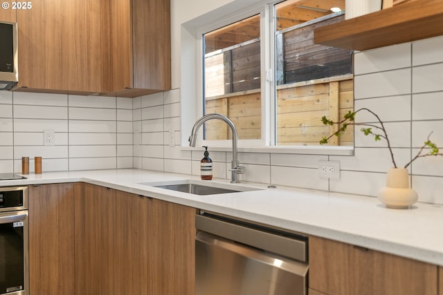 kitchen with brown cabinets, modern cabinets, a sink, appliances with stainless steel finishes, and decorative backsplash