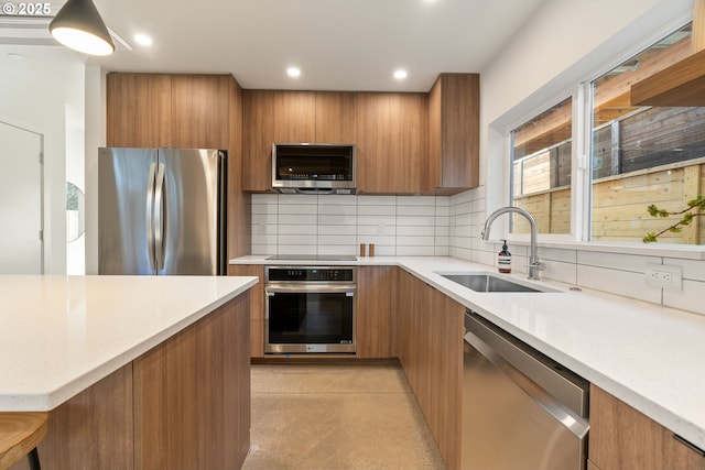 kitchen with backsplash, appliances with stainless steel finishes, brown cabinetry, modern cabinets, and a sink