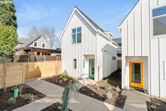 view of front facade with board and batten siding, roof with shingles, and fence