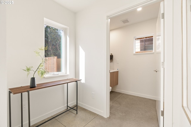 hall with visible vents, concrete floors, and baseboards