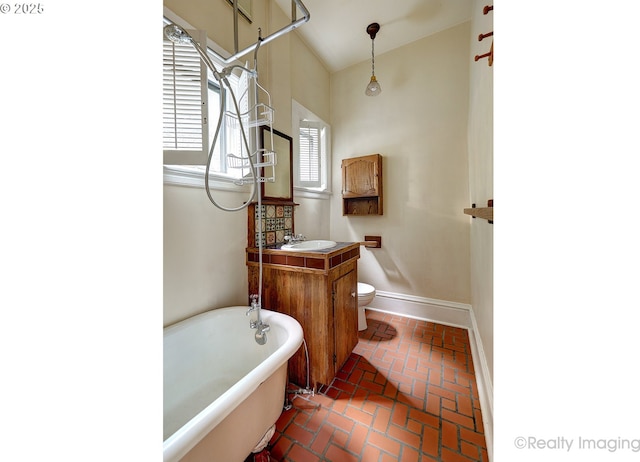 bathroom with a tub to relax in, vanity, lofted ceiling, and toilet