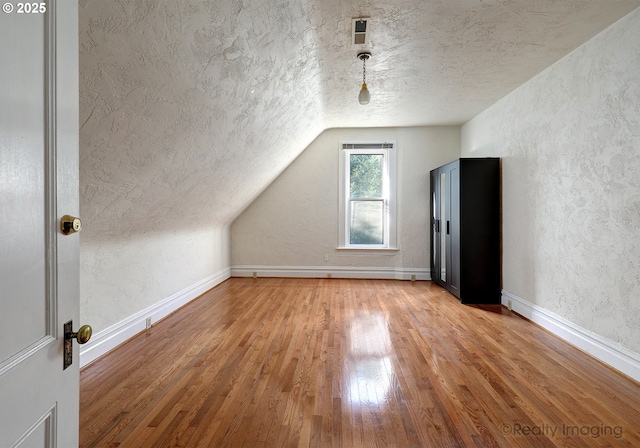 bonus room with lofted ceiling, a textured ceiling, and hardwood / wood-style flooring