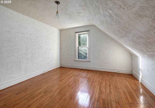 additional living space featuring vaulted ceiling, a textured ceiling, and hardwood / wood-style floors