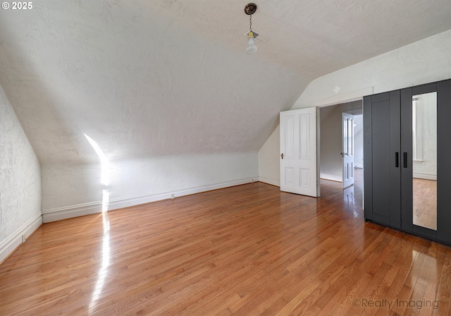 additional living space with lofted ceiling, a textured ceiling, and light hardwood / wood-style flooring