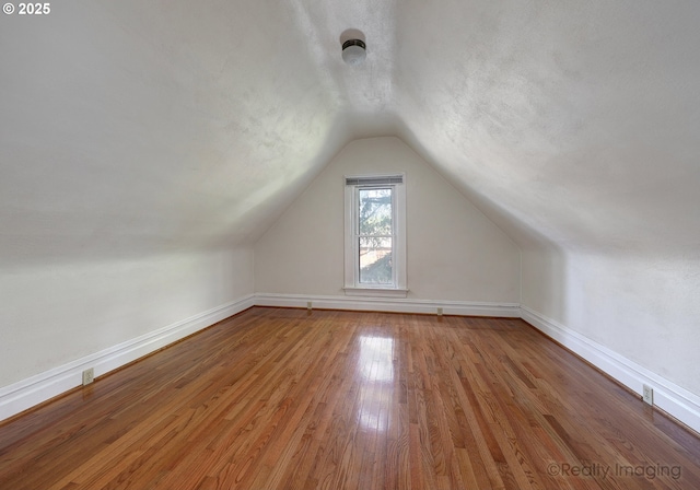 additional living space with lofted ceiling and hardwood / wood-style flooring