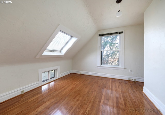 additional living space with lofted ceiling with skylight, a textured ceiling, and hardwood / wood-style floors