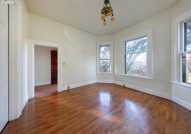 empty room with dark hardwood / wood-style flooring, a wealth of natural light, and a chandelier