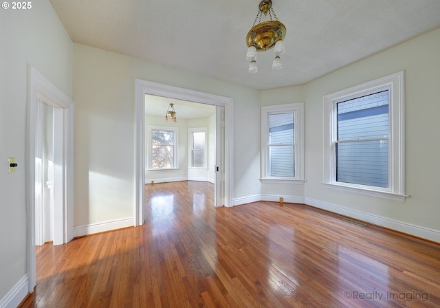 spare room with wood-type flooring and an inviting chandelier