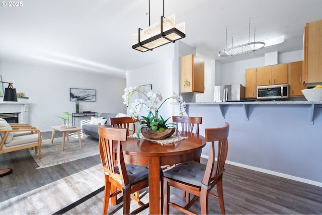 dining area with a fireplace, baseboards, and dark wood-style flooring