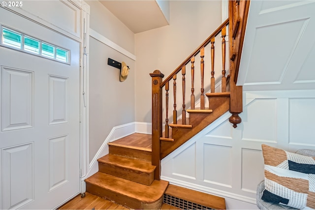 foyer entrance featuring stairs, visible vents, a decorative wall, and wood finished floors