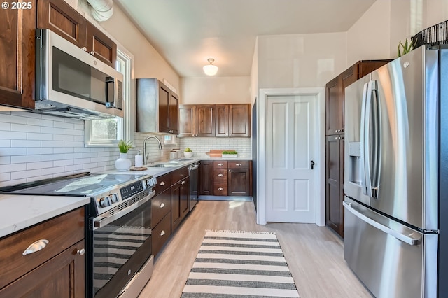 kitchen with decorative backsplash, light wood-style flooring, appliances with stainless steel finishes, dark brown cabinets, and a sink