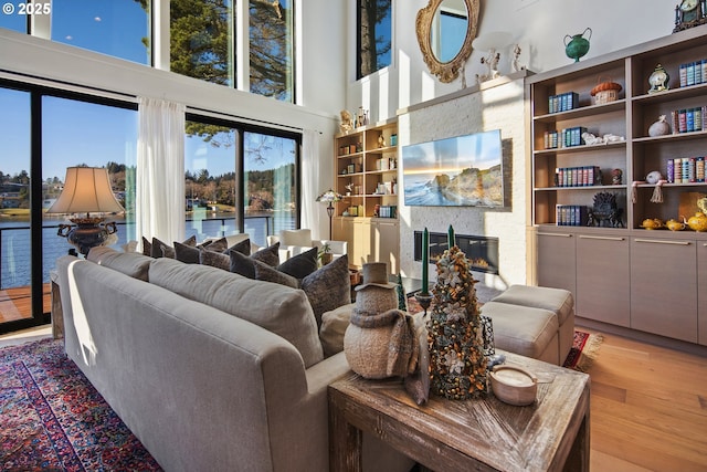 living room featuring a large fireplace, a high ceiling, a water view, and light wood-type flooring