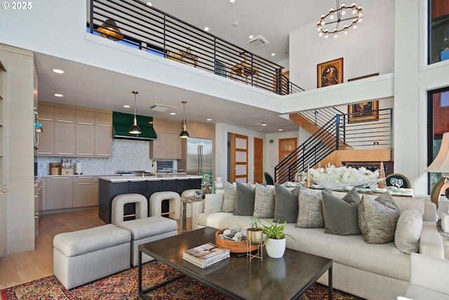 living room with visible vents, a towering ceiling, stairway, recessed lighting, and light wood finished floors