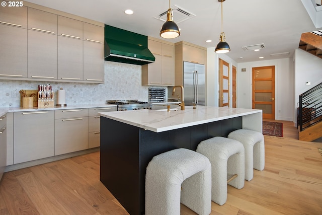 kitchen with a sink, light wood-style flooring, wall chimney exhaust hood, stainless steel built in fridge, and visible vents