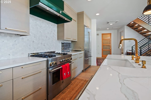 kitchen featuring high quality appliances, a sink, light wood-style flooring, wall chimney exhaust hood, and visible vents