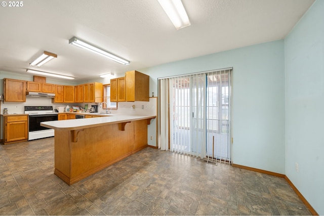 4616 SE 128th Ave, Portland, OR 97236 - kitchen with white range with electric stovetop, under cabinet range hood, light countertops, a peninsula, and dark stone finish floors