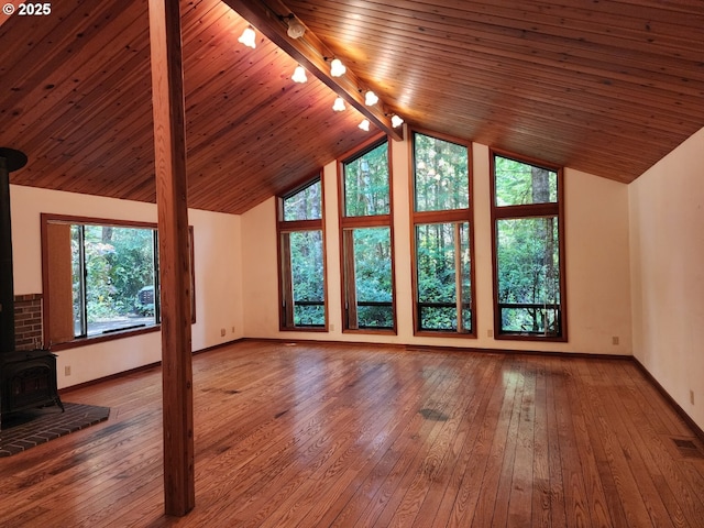 42250 Cedar Hollow Rd, Port Orford, OR 97465 - unfurnished living room featuring a wood stove, track lighting, baseboards, lofted ceiling, and wood-type flooring