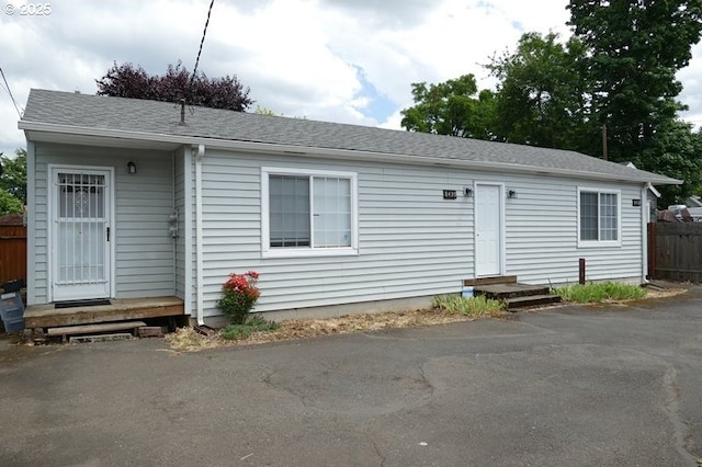 view of front facade with entry steps, fence, and roof with shingles
