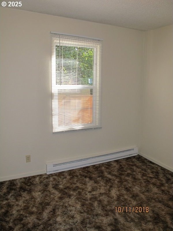empty room with carpet flooring, a baseboard radiator, and baseboards