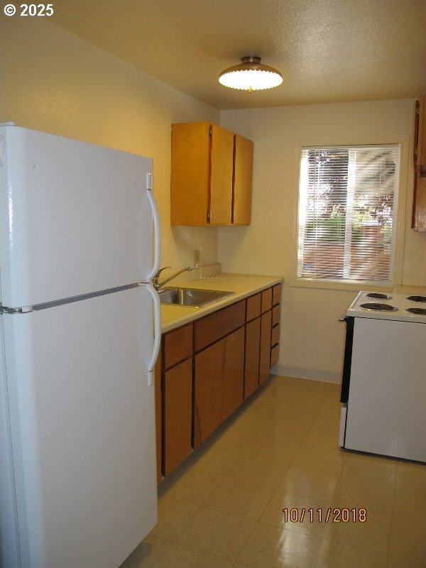 kitchen with baseboards, white appliances, light countertops, and a sink