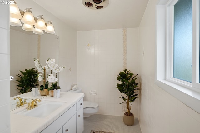 bathroom with toilet, tile patterned flooring, tile walls, and vanity