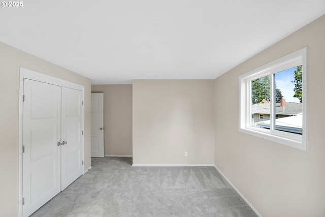 unfurnished bedroom with light carpet, baseboards, and a closet