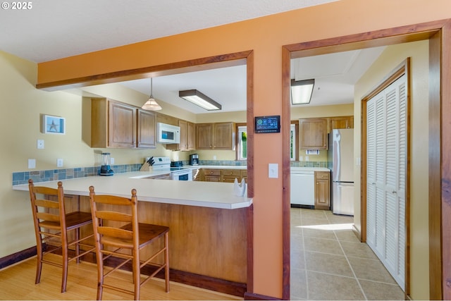 kitchen featuring light tile patterned flooring, hanging light fixtures, a kitchen breakfast bar, kitchen peninsula, and white appliances