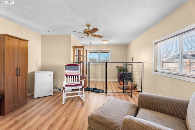 sitting room featuring ceiling fan, light hardwood / wood-style floors, and a textured ceiling