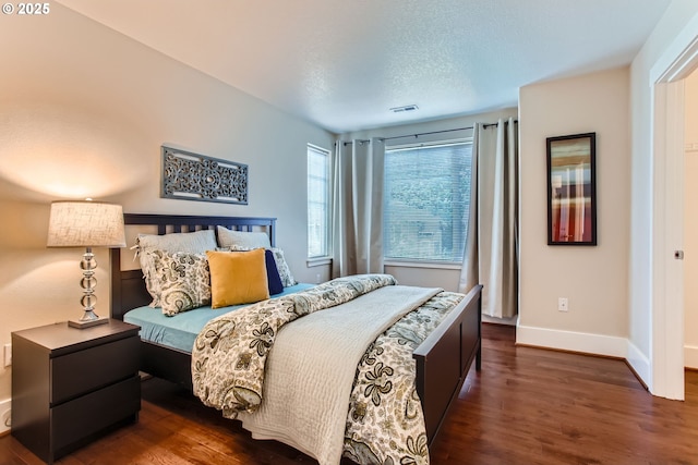 bedroom with a textured ceiling, baseboards, visible vents, and wood finished floors