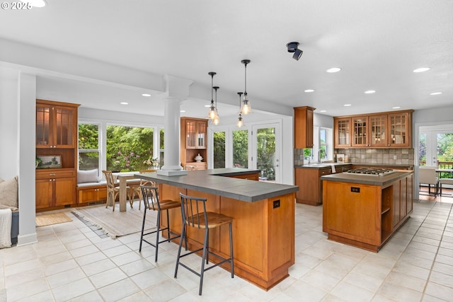 6322 Pony Ct, West Linn, OR 97068 - kitchen featuring ornate columns, brown cabinetry, a center island, dark countertops, and tasteful backsplash