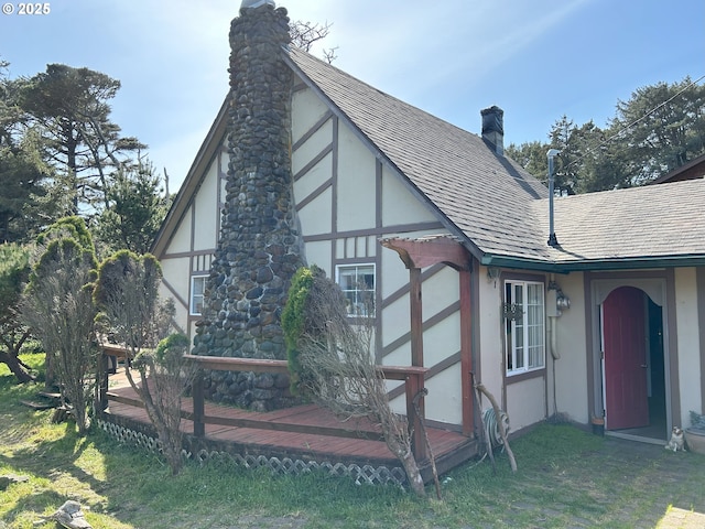 view of home's exterior with roof with shingles, stucco siding, a chimney, and a lawn