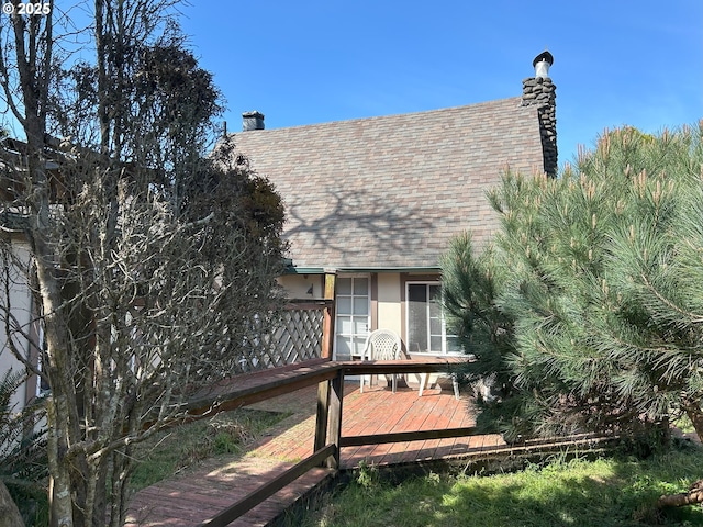 back of house with a shingled roof, a deck, stucco siding, and a chimney