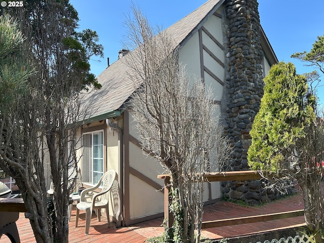 view of side of home featuring a wooden deck, a shingled roof, and stucco siding