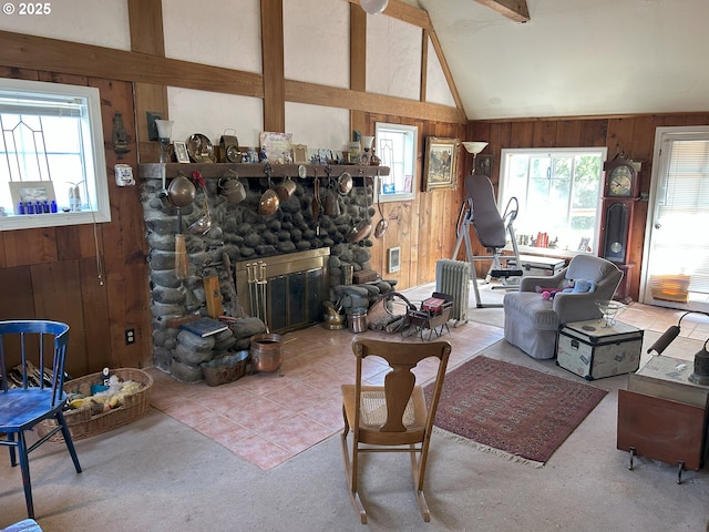 living area with wooden walls, carpet floors, a stone fireplace, and lofted ceiling with beams