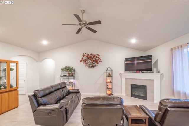 living area with lofted ceiling, ceiling fan, a tiled fireplace, arched walkways, and wood finished floors