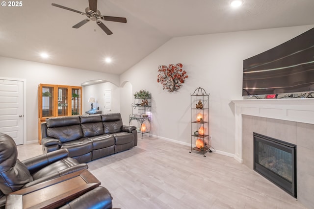 living area with lofted ceiling, a ceiling fan, arched walkways, a tile fireplace, and recessed lighting