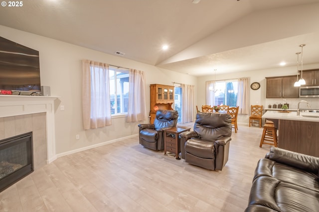 living room with vaulted ceiling, light wood-type flooring, a tile fireplace, recessed lighting, and baseboards