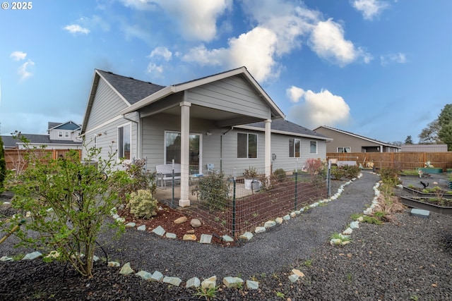 view of front of house featuring a patio area, fence, roof with shingles, and a vegetable garden