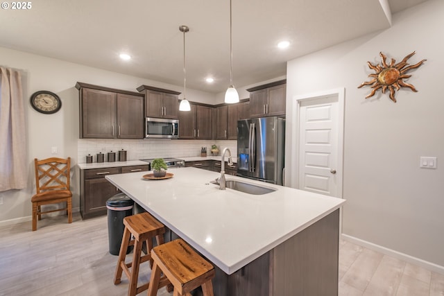 kitchen featuring appliances with stainless steel finishes, a sink, dark brown cabinets, light countertops, and backsplash