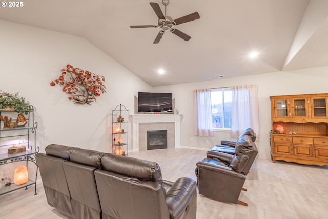 living room featuring vaulted ceiling, light wood-style floors, a ceiling fan, a tiled fireplace, and recessed lighting