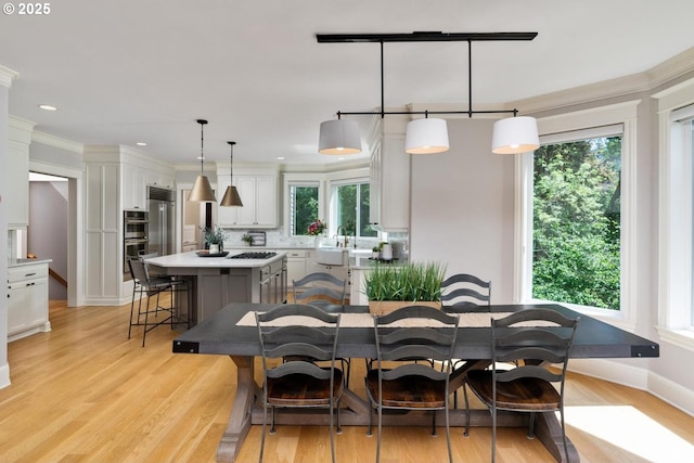 dining area with light wood-type flooring, crown molding, baseboards, and recessed lighting